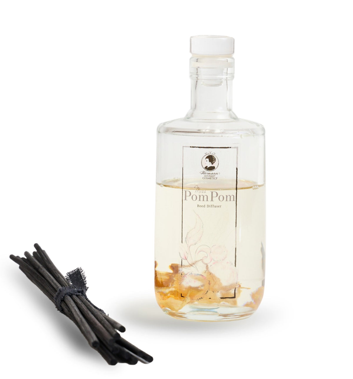 A clear glass diffuser bottle with a label reading 'MISS POM POM', a set of black reeds, and a bit of liquid visible inside the bottle.
