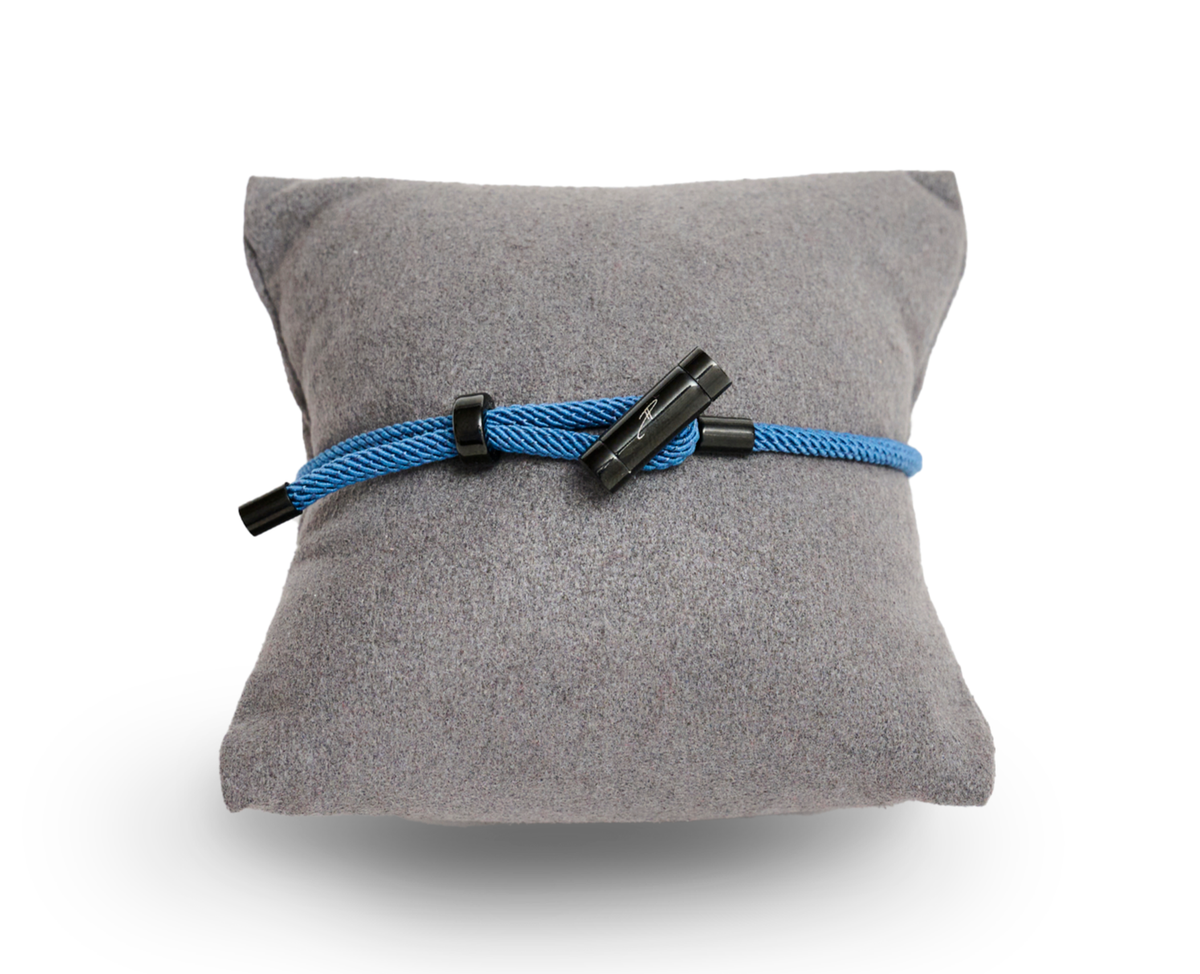 A stainless steel bracelet with a black rhodium plating, featuring a blue ceramic stone, displayed on a grey cushion.